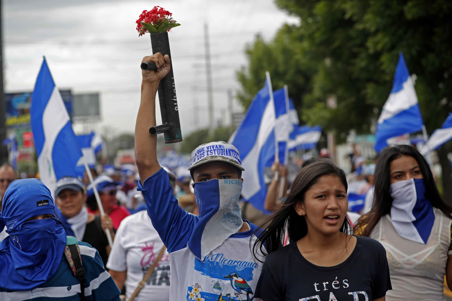 Jóvenes con el rostro cubierto marchando con banderas de Nicaragua durante las protestas de 2018