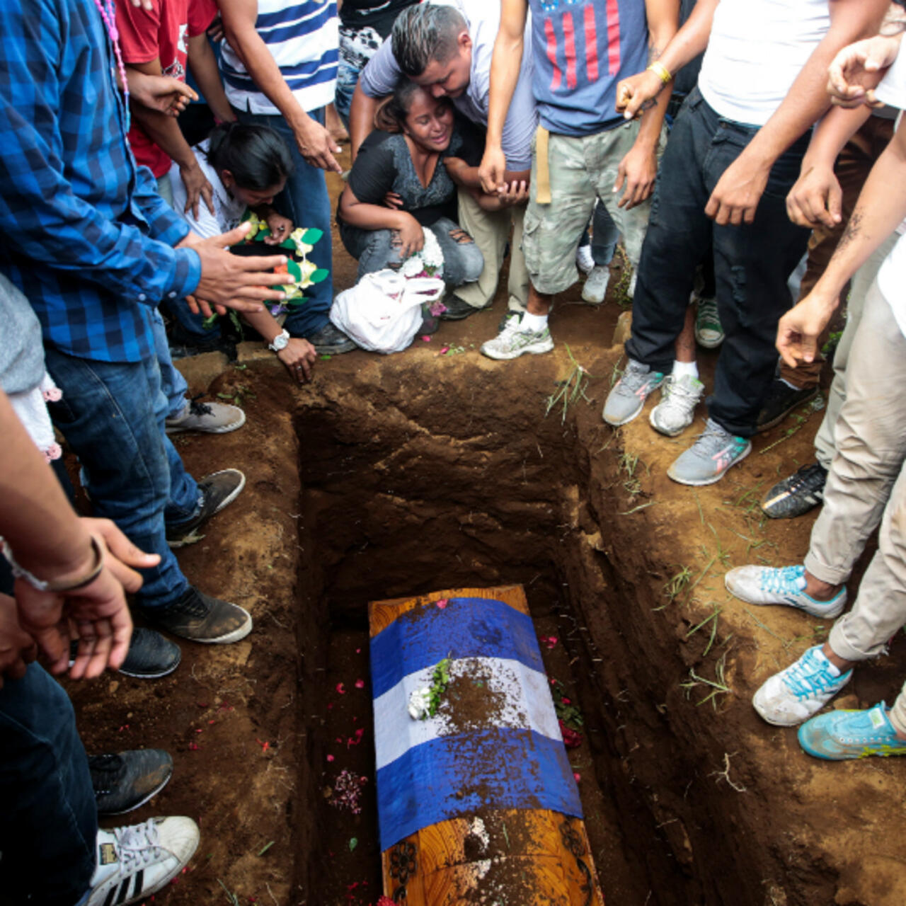 Familiares llorando junto a un ataúd cubierto con la bandera de Nicaragua en un cementerio