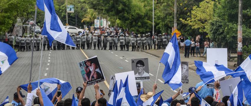 Manifestantes con banderas y retratos de víctimas frente a una fila de policías antimotines