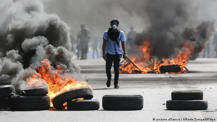 Hombre caminando entre llantas en llamas en una calle durante las protestas de 2018