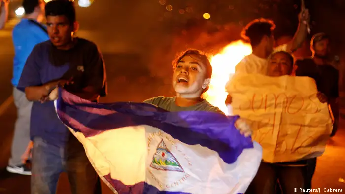 Manifestante sosteniendo la bandera de Nicaragua frente a una hoguera durante una protesta nocturna
