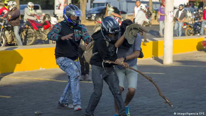 Hombres con cascos golpeando con un palo a un manifestante en la calle