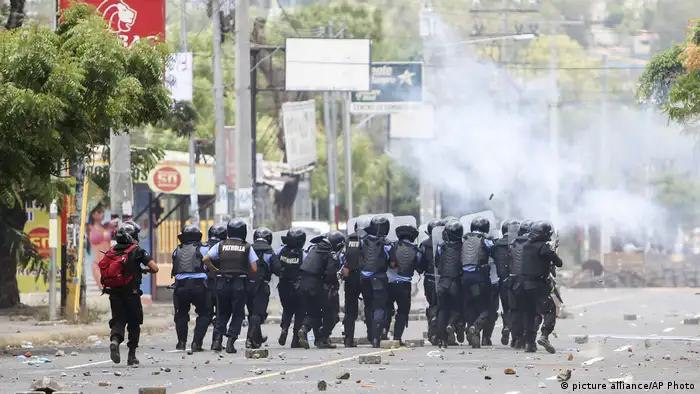 Escuadrón de policías antimotines avanzando por una avenida con gas lacrimógeno