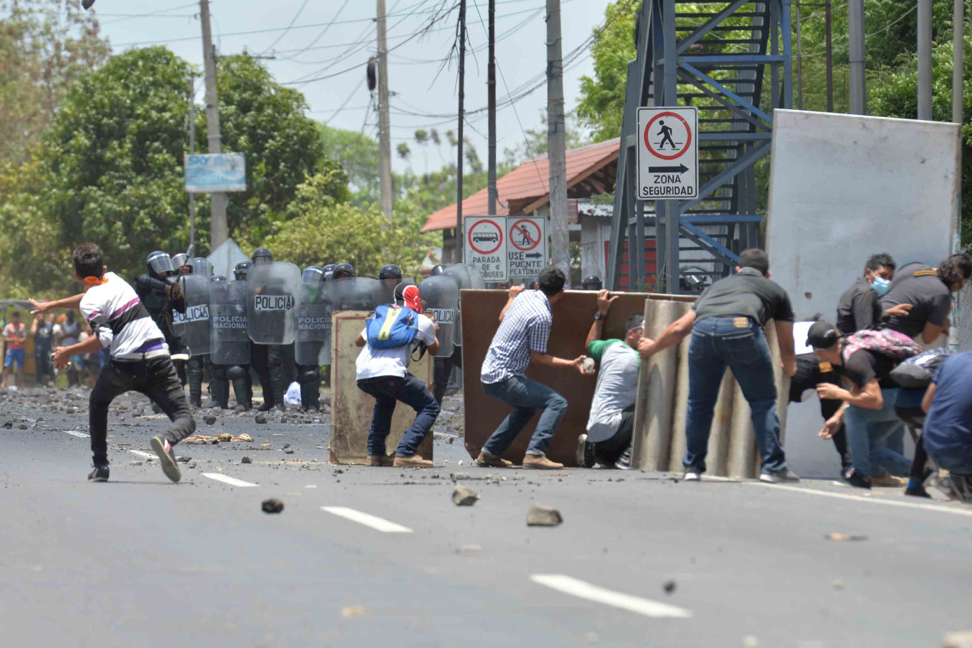 Estudiantes con escudos improvisados enfrentando a policías antimotines en una avenida