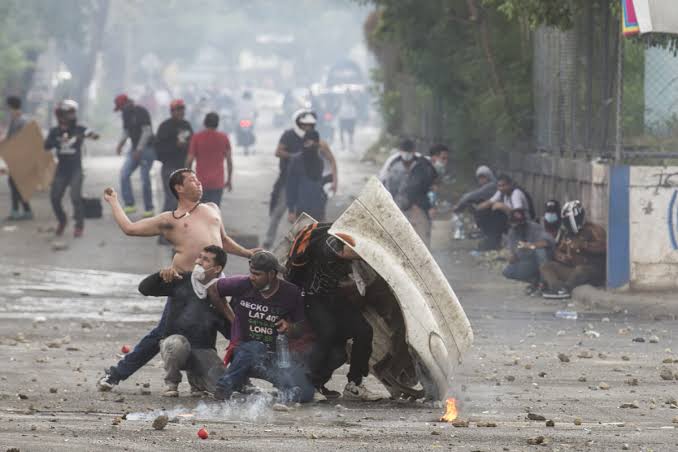 Manifestantes cubriéndose con escudos improvisados entre humo durante un enfrentamiento