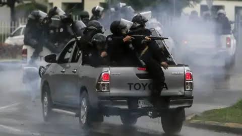 Policías antimotines armados desplazándose en la parte trasera de una camioneta entre gas lacrimógeno